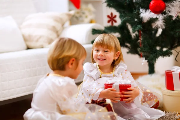Två tvillingar flicka sitter med presenterar nära julgran — Stockfoto