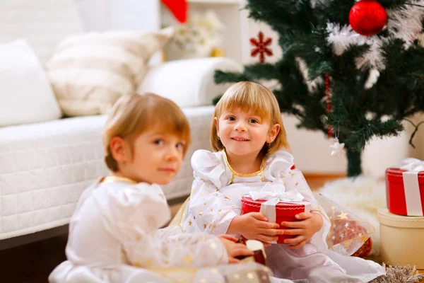 Dvě dívky, které seděly s představuje u vánočního stromu — Stock fotografie
