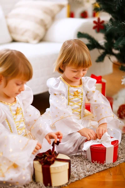 Två glada tvillingar flicka öppning presenterar nära julgran — Stockfoto