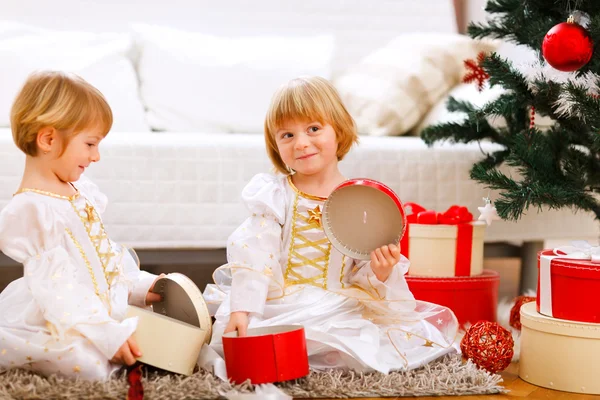 两个微笑着双胞胎女孩打开礼物圣诞节树附近 — 图库照片
