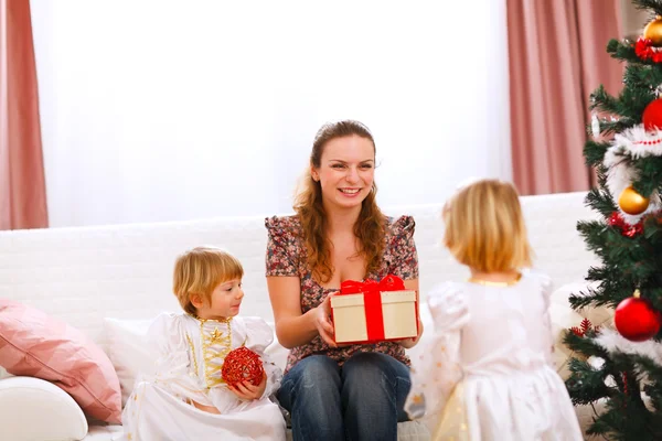 Två tvillingar flicka presentera gåva till mamma nära julgran — Stockfoto