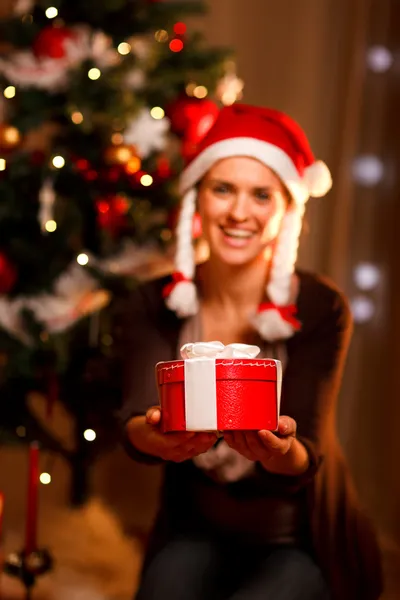 Smiling woman near Christmas tree presenting gift box. Focus on Stock Photo