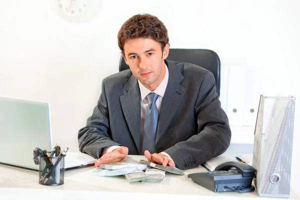 Modern businessman sitting at office desk and giving money packs — Stock Photo, Image