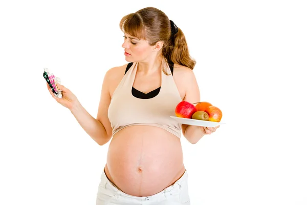 Mujer embarazada pensativa eligiendo entre drogas y frutas Imagen De Stock
