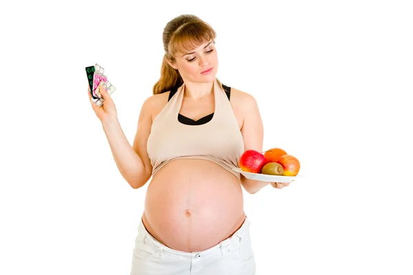 Fundersam gravid kvinna att göra valet mellan piller och frukter Stockfoto