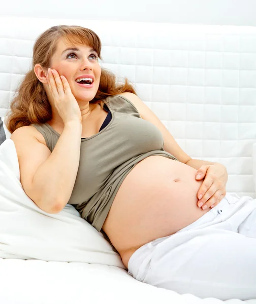 Happy beautiful pregnant woman sitting on sofa and holding her belly — Stock Photo, Image