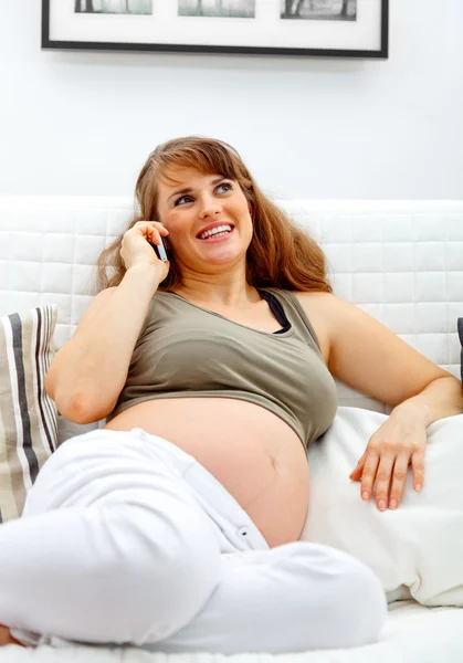 Smiling beautiful pregnant woman sitting on sofa and talking mobile phone. Royalty Free Stock Images