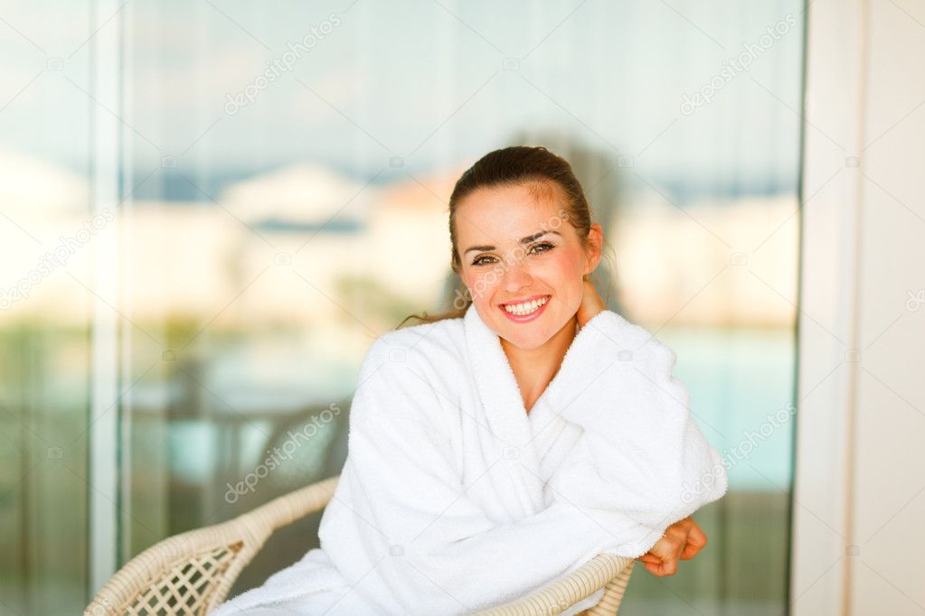 Portrait of lovely smiling woman in bathrobe sitting at terrace
