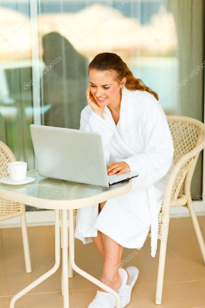 Smiling attractive female in bathrobe sitting at table on terrac