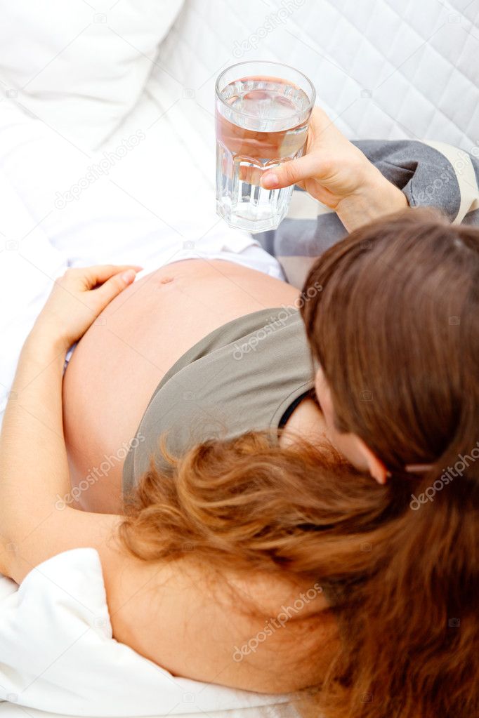 Pregnant woman relaxing on sofa with glass of water in hand. Close-up.