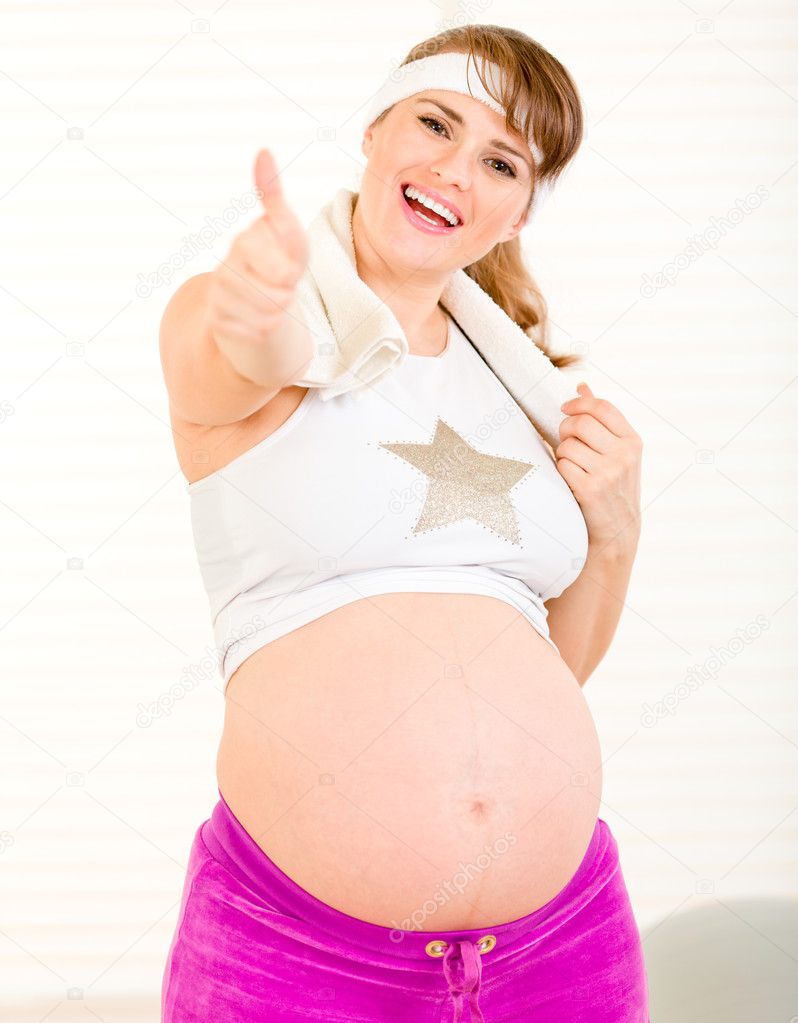 Happy pretty pregnant woman in sportswear showing thumbs up gesture