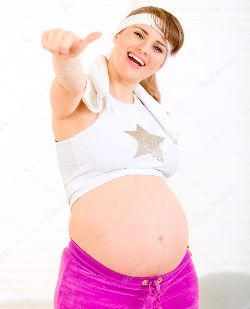 Smiling beautiful pregnant woman in sportswear showing thumbs up gesture