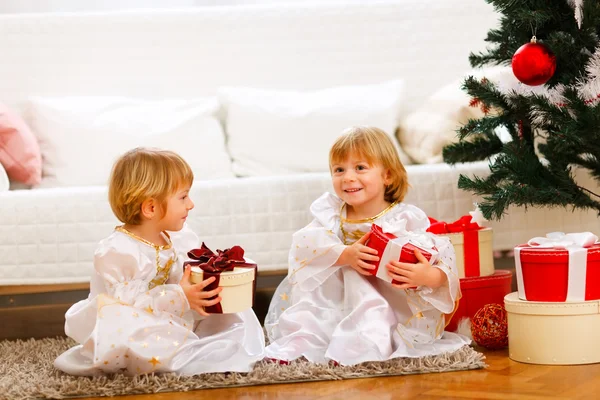 Två tvillingar flicka sitter med presenterar nära julgran — Stockfoto