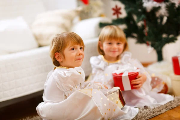 Två tvillingar flickorna sitter med presenterar nära julgran — Stockfoto