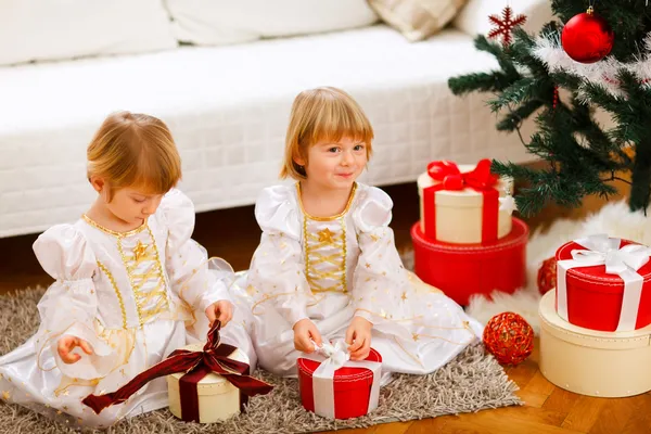 Två söta tvillingar flickor öppna presenterar nära julgran — Stockfoto