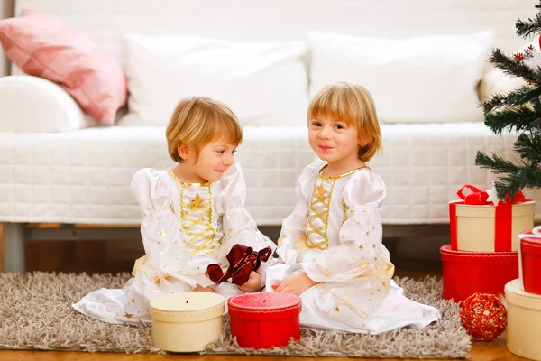 Twee tweelingen meisjes zitten met in de buurt van de kerstboom presenteert — Stockfoto