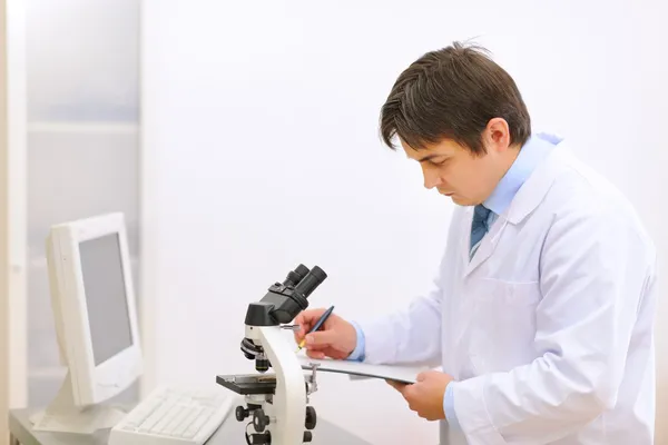 Researcher using microscope in medical laboratory and taking not — Stock Photo, Image
