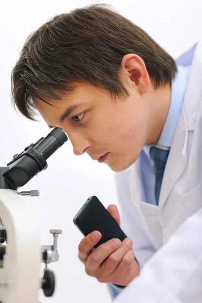 Investigador mirando en el microscopio y tomando notas en el recor de voz — Foto de Stock