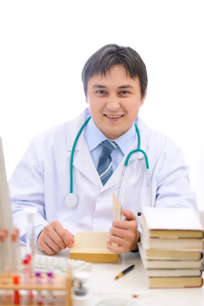 Médico sorridente sentado à mesa e lendo livro — Fotografia de Stock