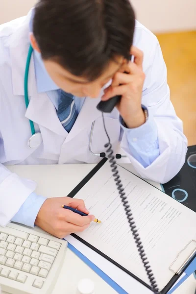 Arzt spricht Telefon und Notizen in der Zwischenablage. Ansicht von oben — Stockfoto