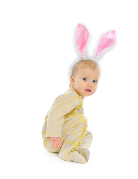 Bebê bonito com orelhas de coelho sentado no chão isolado em branco — Fotografia de Stock