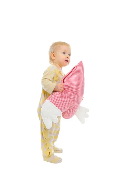 Interested baby standing with heart shaped pillow and looking in — Stock Photo, Image