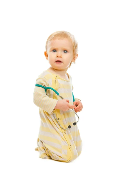 Confused baby with stethoscope sitting on floor isolated on whit — Stock Photo, Image