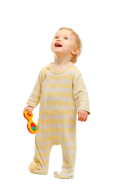 Lindo bebé de pie con sonajero y mirando hacia arriba aislado en blanco — Foto de Stock
