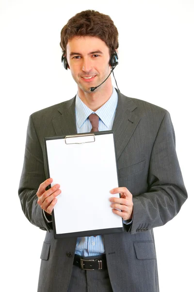 Sonriente hombre de negocios moderno en auriculares que muestran portapapeles en blanco — Foto de Stock