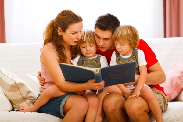 Mother and father looking photo album with twins daughters — Stock Photo, Image