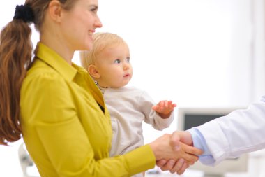 Closeup on mother with baby thanking pediatrician doctor for exa clipart