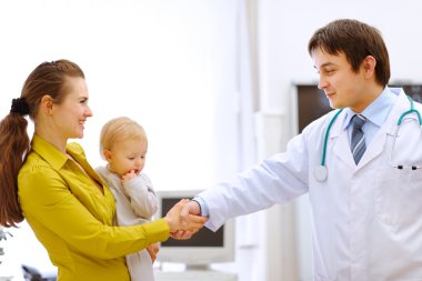 Mother holding baby and handshaking pediatric doctor's hand clipart