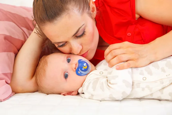 Kanepede döşenmesi ve bebek öpüşme genç anne — Stok fotoğraf