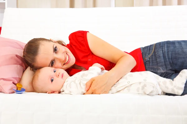 Smiling mother with baby laying on couch — Stock Photo, Image