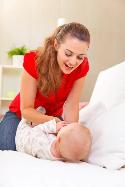Jonge moeder spelen met baby op divan — Stockfoto