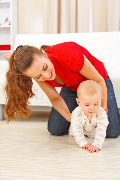 Madre ayudando a bebé alegre aprender a arrastrarse —  Fotos de Stock