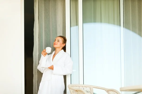 Mulher encantadora em roupão de banho de pé perto de grandes janelas do quarto e havi — Fotografia de Stock
