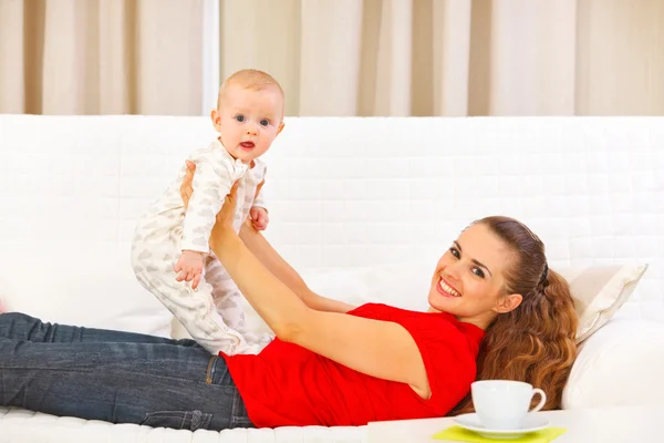 Улыбающаяся мать и очаровательный ребенок играют на диване — стоковое фото