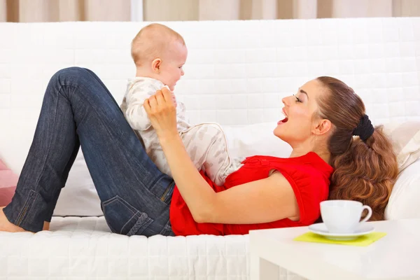 Sonriente madre y lindo bebé jugando en diván — Foto de Stock