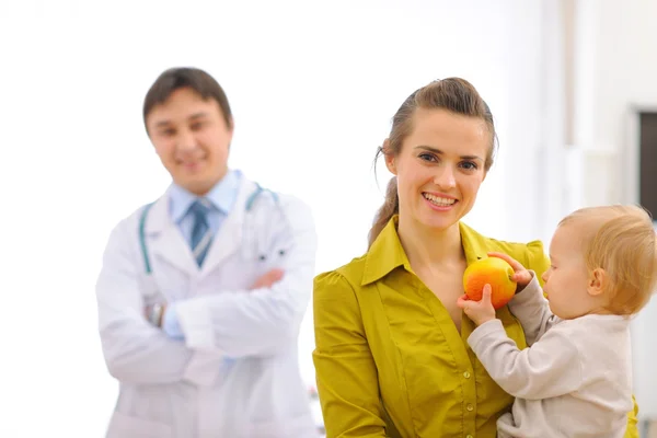 Портрет матері з дитиною, що тримає яблуко і лікаря на фоні — стокове фото