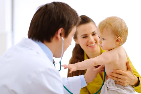 Interested baby stretching for stethoscope while being on examin Stock Image