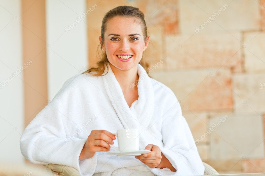 Beautiful woman in bathrobe sitting at table on terrace and havi