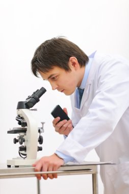 Researcher looking in microscope and making notes on voice recor clipart