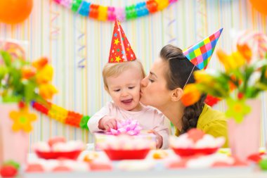 Mother kissing her happy while baby checking present clipart