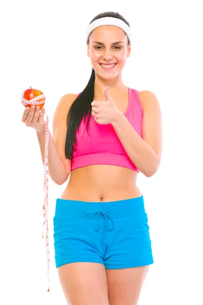Chica sana sosteniendo manzana con cinta métrica y mostrando el pulgar — Foto de Stock