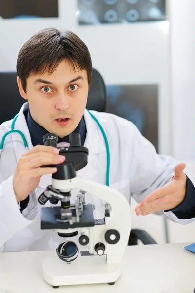 Förvirrad manliga forskare pekar på mikroskopet — Stockfoto