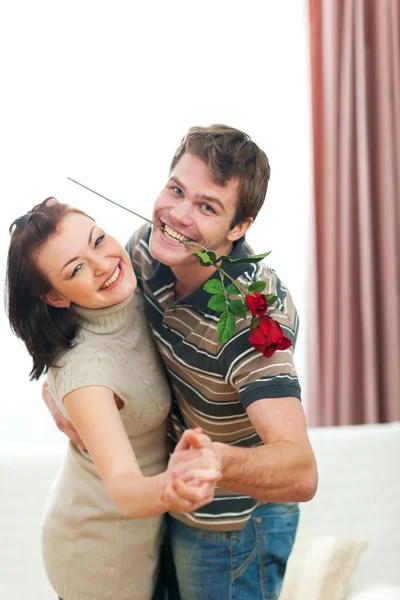 Feliz jovem casal dançando com rosa vermelha em casa — Fotografia de Stock