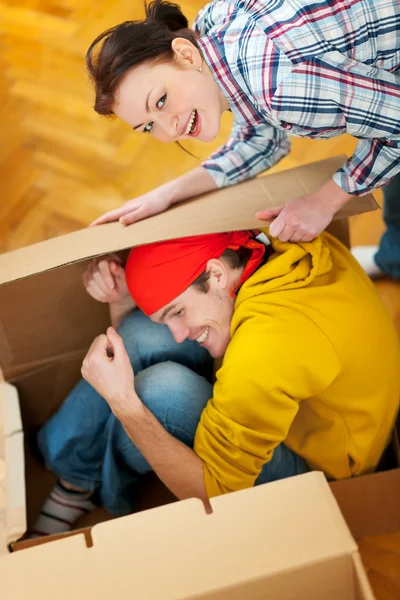 Smiling girl trying to pack boyfriend in cardboard box — Stock Photo, Image