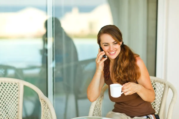 Gelukkig meisje mobiele telefoon spreken en met kop koffie in terra — Stockfoto
