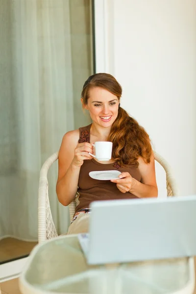 Νεαρή γυναίκα με τον καφε και ψάχνει σε φορητό υπολογιστή στη βεράντα — Φωτογραφία Αρχείου